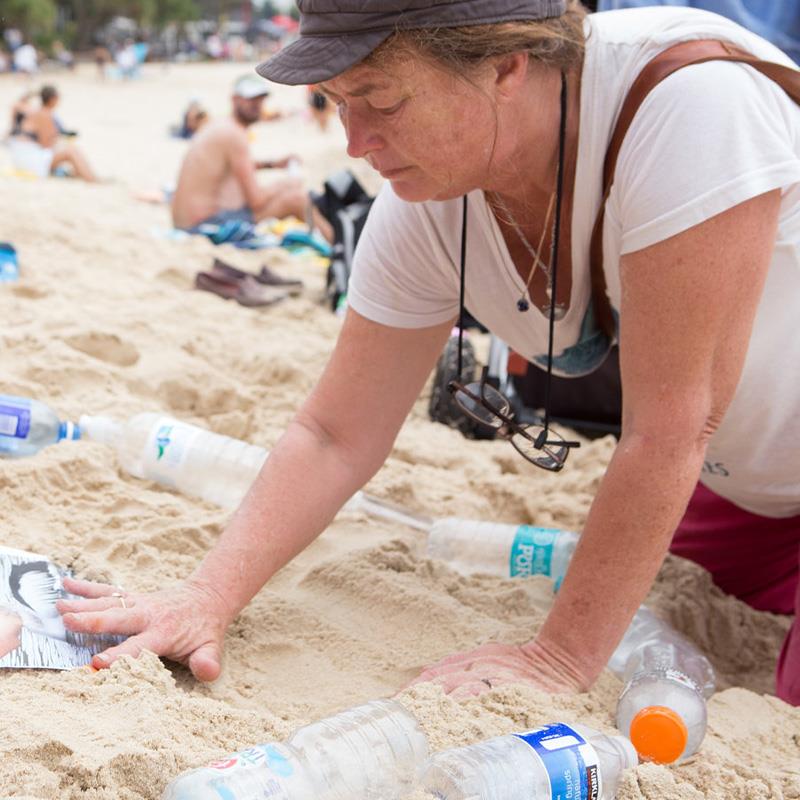 woman picking up plastic bottles off beach